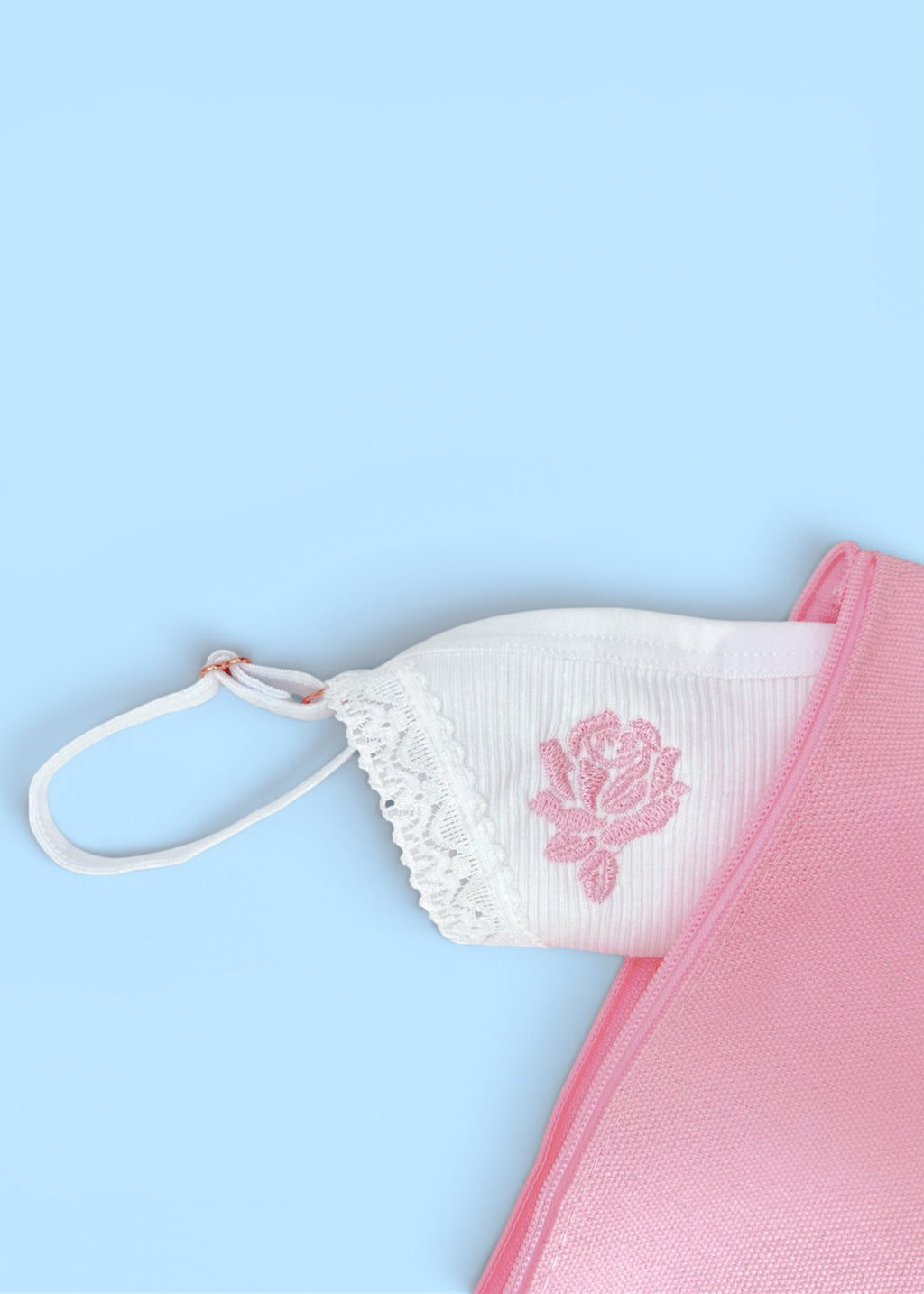 A close up of Berry Sorbet’s Sugar Rose white ribbed cotton thong with a light pink Rose embroidered on the front, with a light blue background and a pink canvas pouch as decoration.
